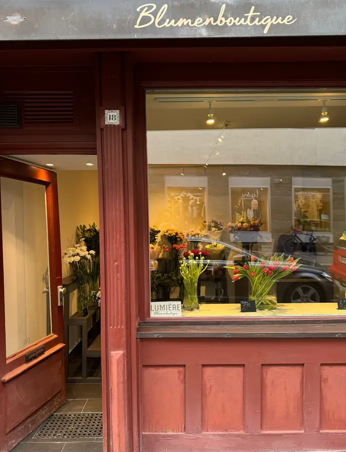 Die rote Holzfassade der Lumière Blumenboutique mit Schriftzug „Blumenboutique“, Hausnummer 18 und Tulpen im Schaufenster