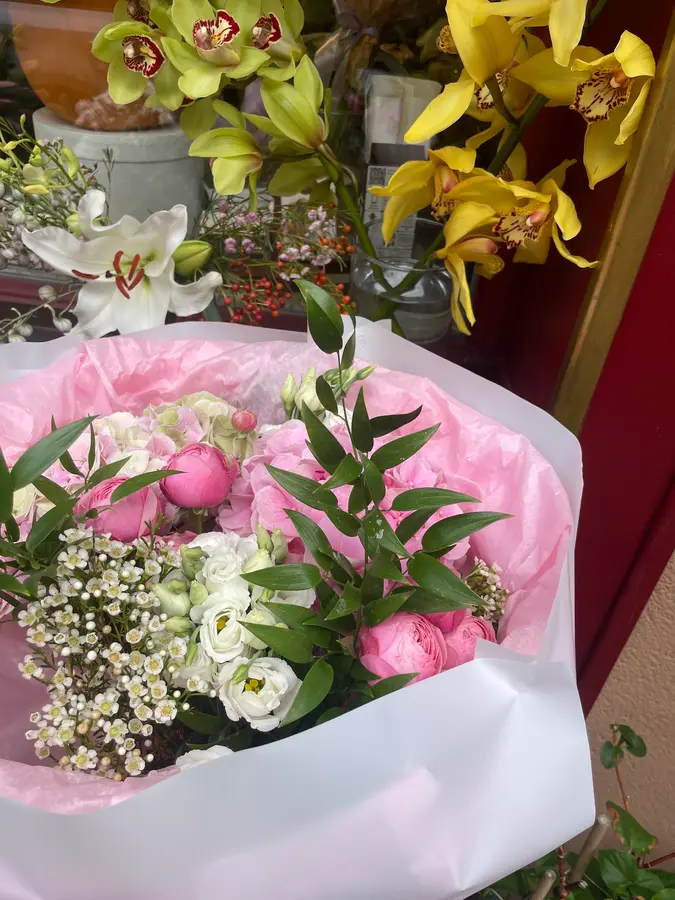 Rosa-weißer Strauß im Laden vor gelben Orchideen und Lilien