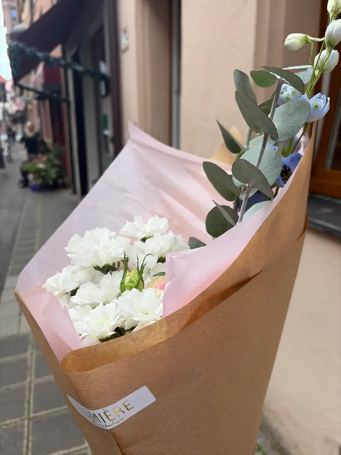 Strauß mit weißen Chrysanthemen und Eukalyptus in Kraftpapier mit dem Lumière-Etikett